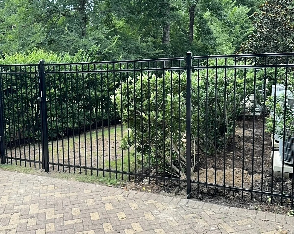 Black ornamental steel fence along a brick patio and wooded garden